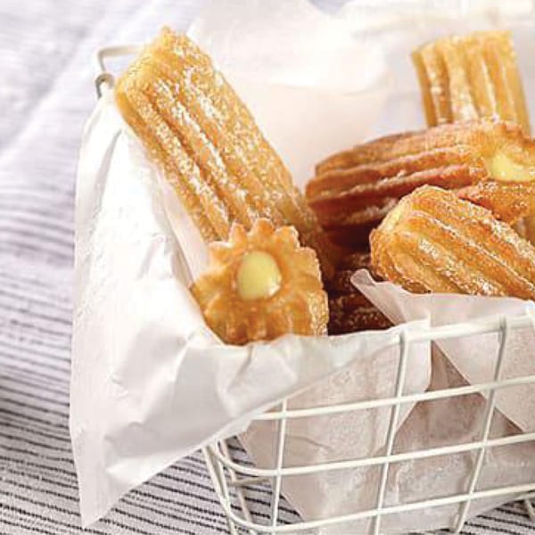 A white wire basket filled with churros, some powdered with sugar, one filled with cream.