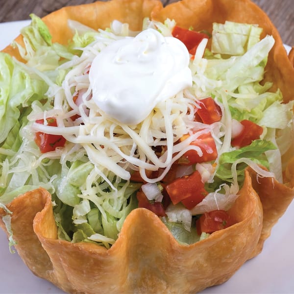 Crispy taco salad bowl filled with shredded lettuce, diced tomatoes, cheese, and a dollop of sour cream.