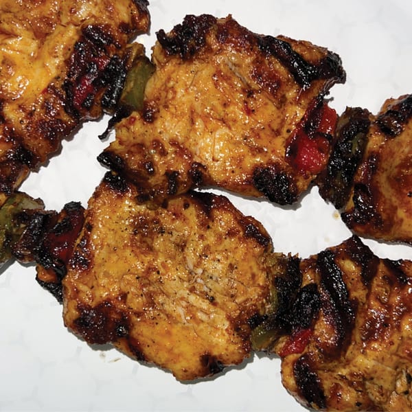 Grilled chicken and vegetable skewers with charred marks on a white background.