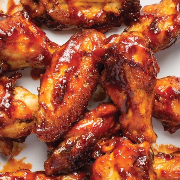 Close-up of several chicken wings coated in a glistening, dark red barbecue sauce.