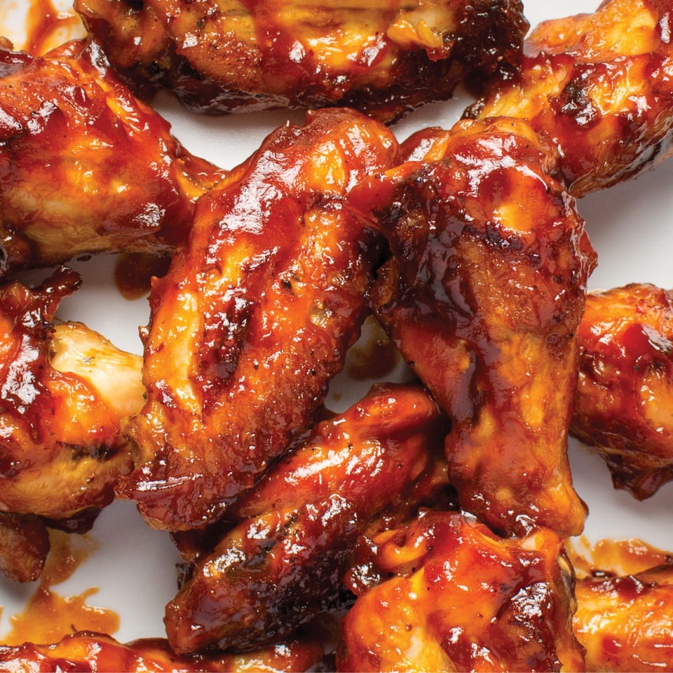 Close-up of several chicken wings coated in a glistening, dark red barbecue sauce.