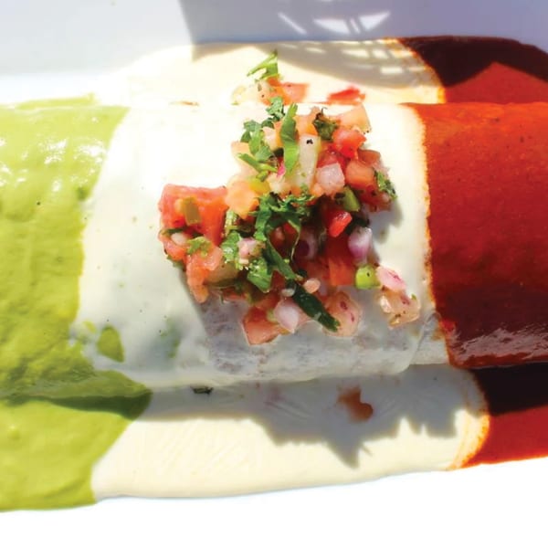 Mexican burrito covered in green, white, and red sauces, topped with fresh pico de gallo.