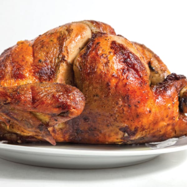 Whole roasted chicken, golden brown and seasoned, on a white plate against a white background.