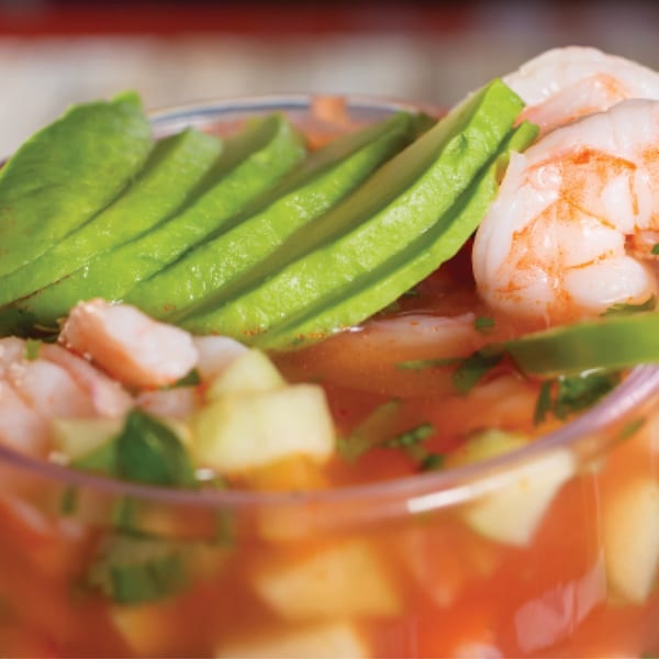 Close-up of Mexican shrimp cocktail with sliced avocado, shrimp, and diced vegetables in a red sauce.