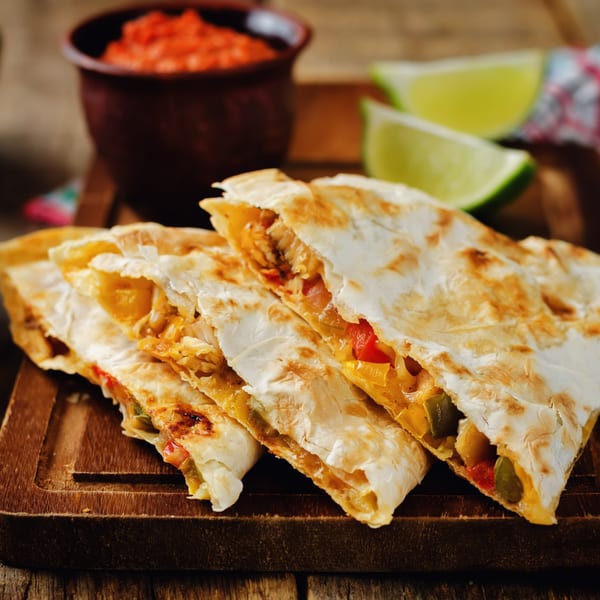 Chicken quesadillas with melted cheese, bell peppers, and onions, served with salsa and lime wedges.